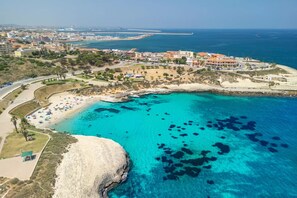 An aerial view of a coastal area with a beach, clear blue waters, and a residential area with buildings. - Panoramic sea View Apartment in Porto Torres (Porto Torres)