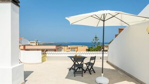 Un balcon avec une table et des chaises, un parasol et une vue sur la mer.