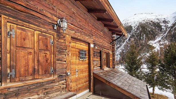 A wooden log cabin with a sloped roof, wooden doors, and a stone entrance.