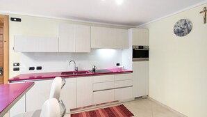 A modern kitchen with white cabinets, a red countertop, and a clock on the wall.