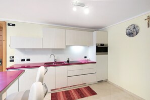 A modern kitchen with white cabinets, a red countertop, and a clock on the wall. - Apartment 'Tea Da Anna E Luigi' with Mountain View, Private Garden and Wi-Fi (Livigno)