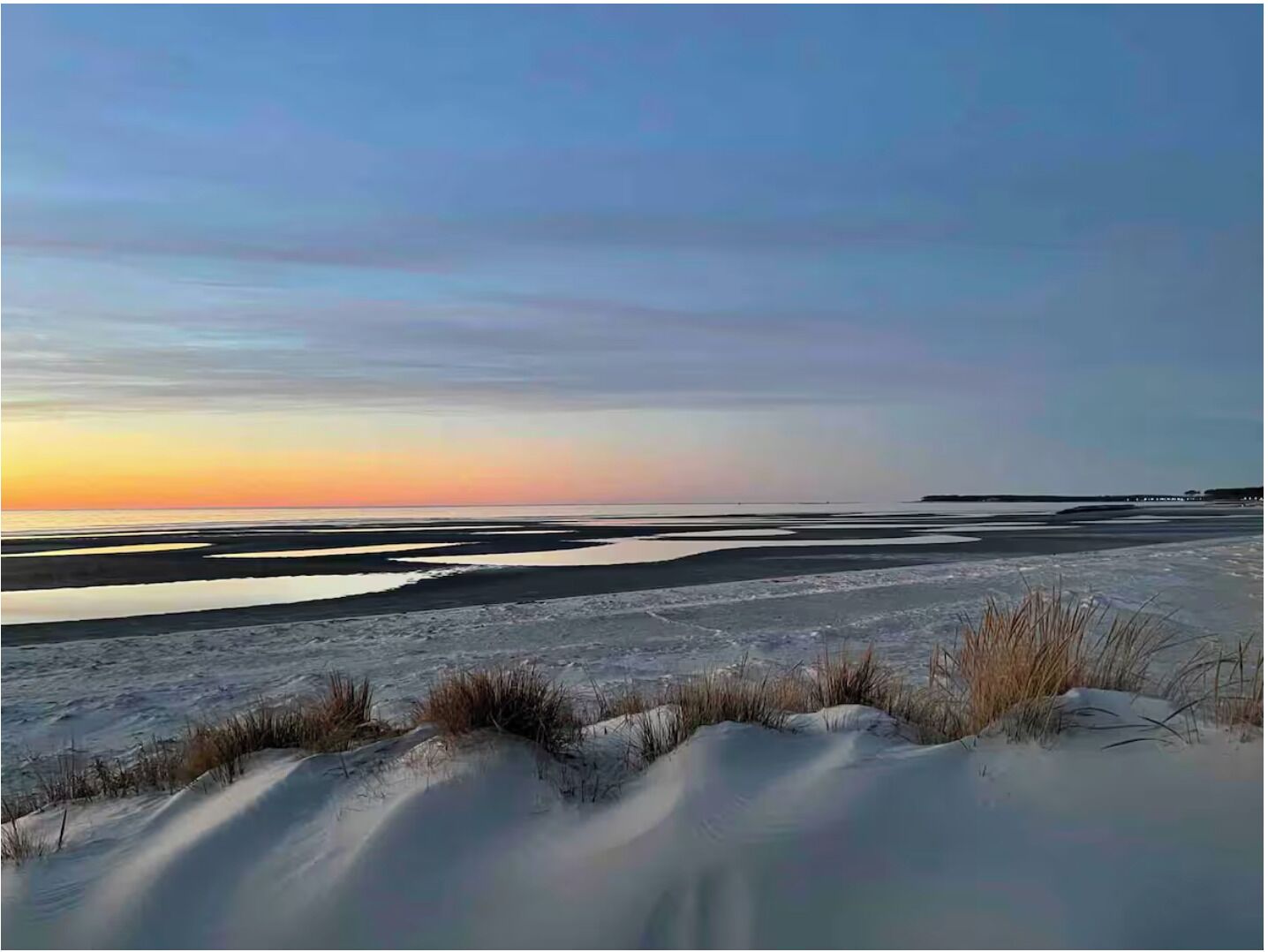 Ett kustlandskap med sanddyner och ett stilla hav under solnedgången.