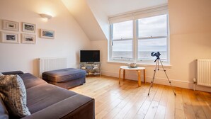 Ein modernes Wohnzimmer mit großem Fenster, einem Flachbildfernseher, einem Stativ und einem gemütlichen Sofa.
