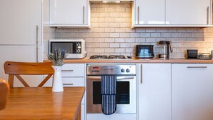Eine moderne Küche mit weißen Schränken, einer Ziegelrückwand, einem eingebauten Backofen, einer Mikrowelle, einer Kaffeemaschine und einem Holzespeisetisch mit einem Blumentopf.