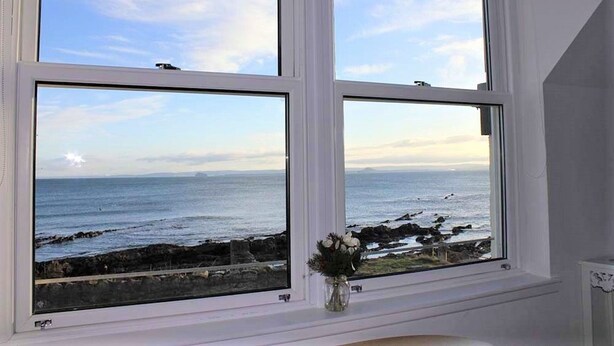 Ein Zimmer mit großem Fenster mit Blick auf eine felsige Küstenlinie und das Meer.
