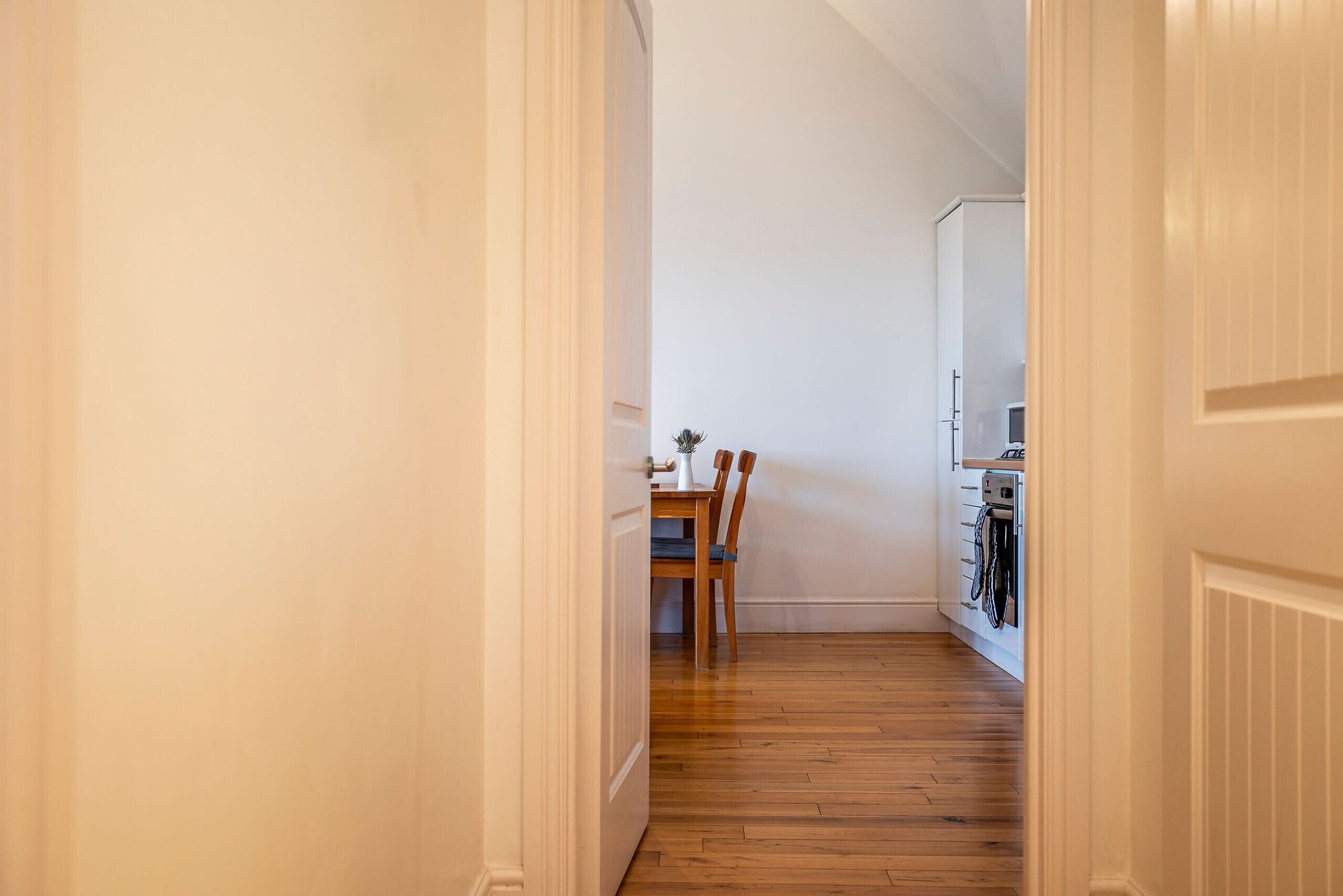 Un pasillo estrecho con suelo de madera que conduce a un comedor con una mesa y sillas.