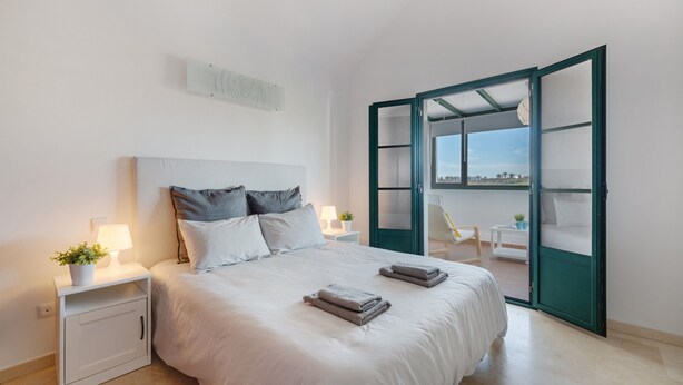 Een slaapkamer met een bed, nachtkastjes, een lamp, een plant in pot en uitzicht door een glazen deur.