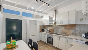 Een moderne keuken met witte kastjes, een ingebouwde oven, een magnetron en een koffieapparaat.