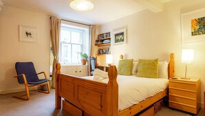 Un dormitorio con una cama de madera, mesitas de noche, una silla, una estantería y una ventana con cortinas.