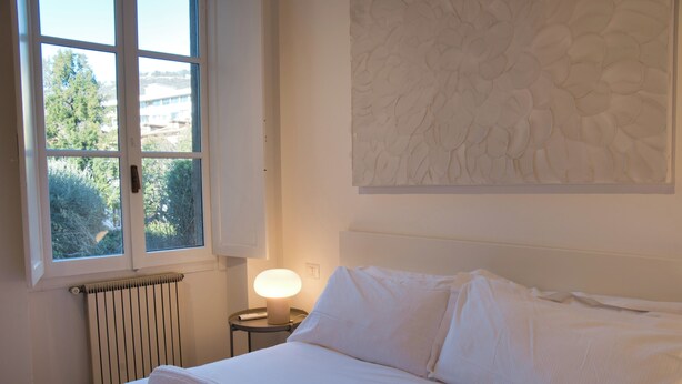 Ein Hotelzimmer mit einem großen Bett, einem Fenster mit Blick auf Bäume, einem Heizkörper und einem Wandbild.