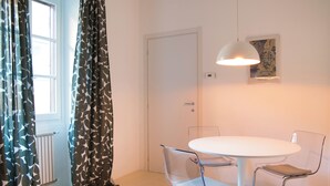 Ein Zimmer mit rundem Tisch, zwei Stühlen, einer Pendelleuchte, einer Tür und einer Heizung.