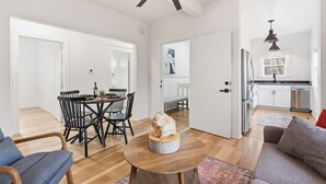 A spacious living area with a dining table, chairs, a round coffee table, and a sofa. There is a kitchen area with a refrigerator, stove, and sink. The room has hardwood flooring and white walls. - Mathews House 4 King Beds Near CSU & Old Town (Fort Collins)