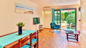 A dining area with a wooden table and chairs, a potted plant, a flat-screen TV, and a view of the outdoors through a glass door. - Very nice app 150m from the beach 50m from the pool (Saint-Raphaël)