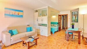 A living room with a sofa, coffee table, and a painting of sailboats. There is a dining area with a table and chairs. - Very nice app 150m from the beach 50m from the pool (Saint-Raphaël)