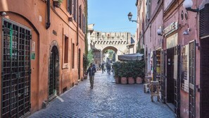 A cobblestone street with buildings on either side, a pedestrian walkway, and an archway in the distance. - Scala Suite (Rome)