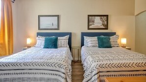 Habitación doble con dos camas, cada una con ropa de cama y almohadas estampadas, ventilador de techo y cuadros en la pared.