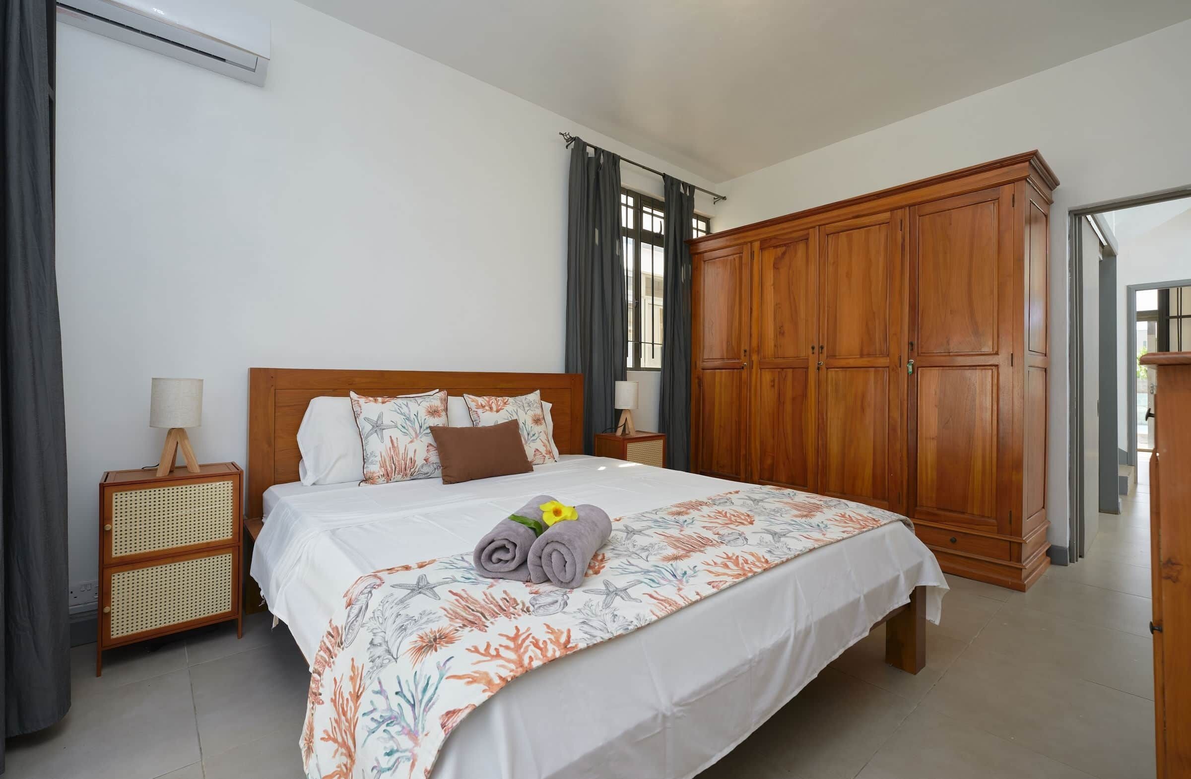 Een slaapkamer met een bed, een houten garderobe, een nachtkastje met een lamp en een raam met gordijnen.