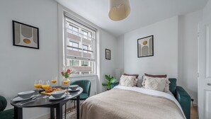 Une chambre moderne avec un grand lit, une table à manger avec des aliments pour le petit-déjeuner, et une fenêtre donnant sur des immeubles.