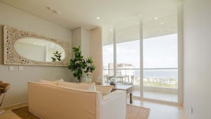 Een moderne woonkamer met een witte bank, een grote spiegel en een stadszicht door ramen van de vloer tot aan het plafond.