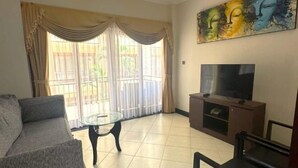 A living room with a sofa, a glass coffee table, a TV on a wooden stand, and a painting on the wall. - Kuta Town Houses (Bali)