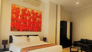 A hotel room with a large bed, a sofa, a coffee table, and a painting on the wall. - Kuta Town Houses (Bali)