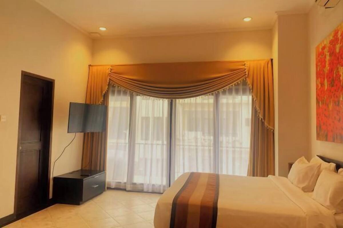 A hotel room with a bed, a TV, a desk, and a window with curtains.