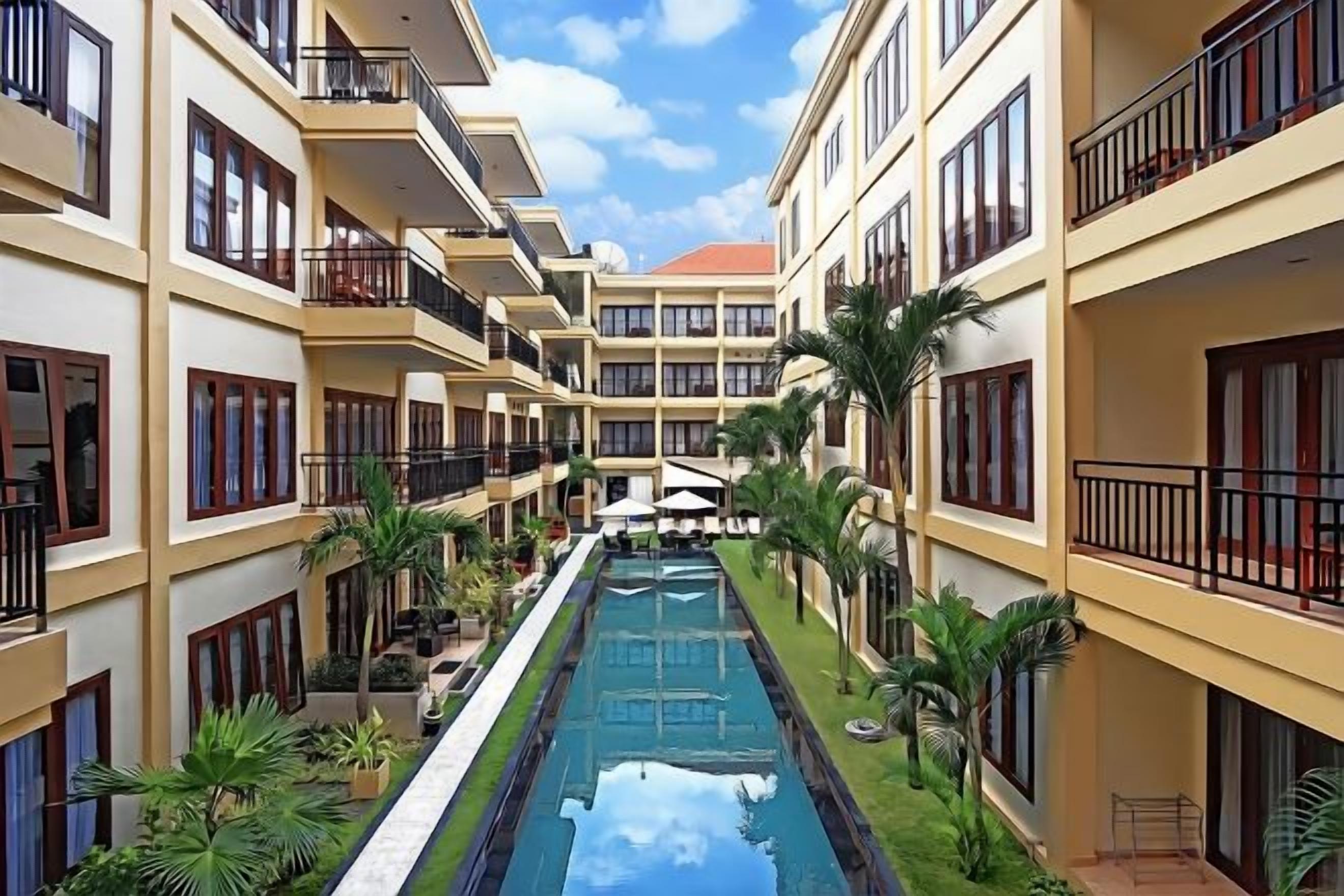 Une cour d’hôtel avec une piscine, de nombreux balcons et des palmiers.