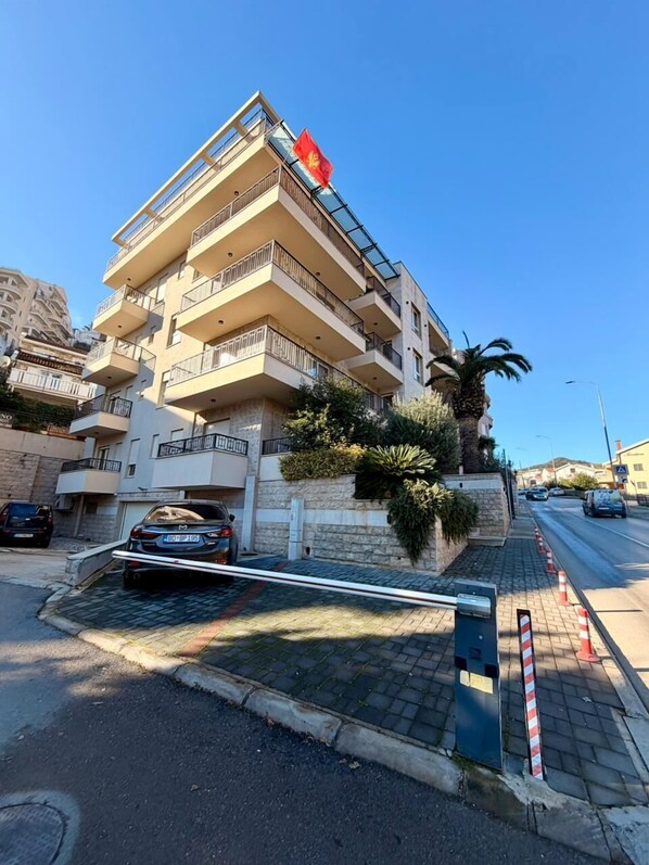 A multi-story residential building with balconies, a palm tree, and a parked car. - LV Central Apartment-Free Parking (Budva)
