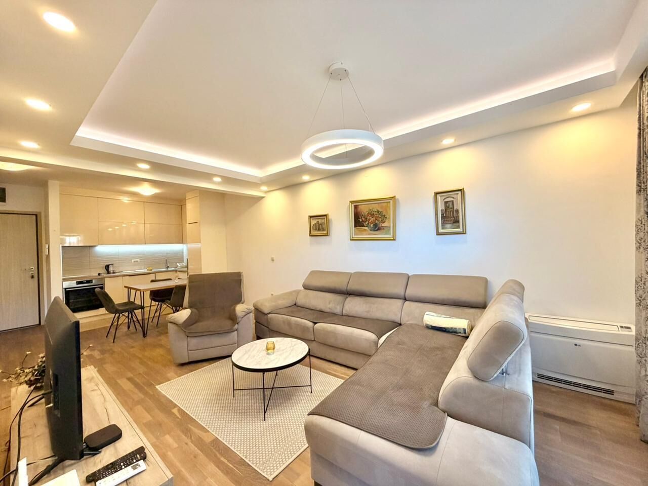 A modern living room with a sectional sofa, a TV, and a dining area with chairs and a table.