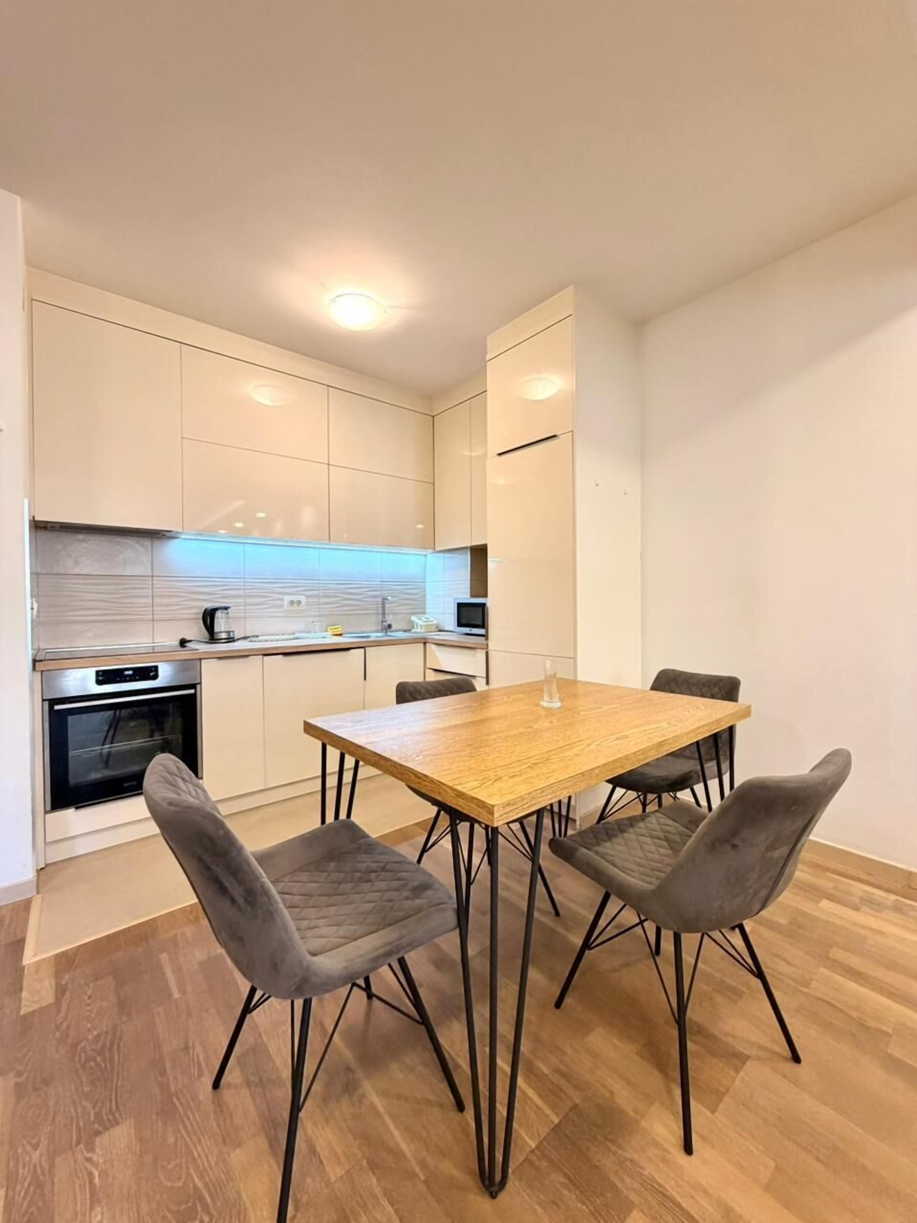 A compact kitchen with a dining area, featuring a wooden table and four chairs, a built-in oven, and a microwave.