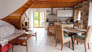 Un salon chaleureux avec un canapé, une table basse et un coin repas comprenant des chaises et une table en osier, le tout préparé pour un dîner à deux.