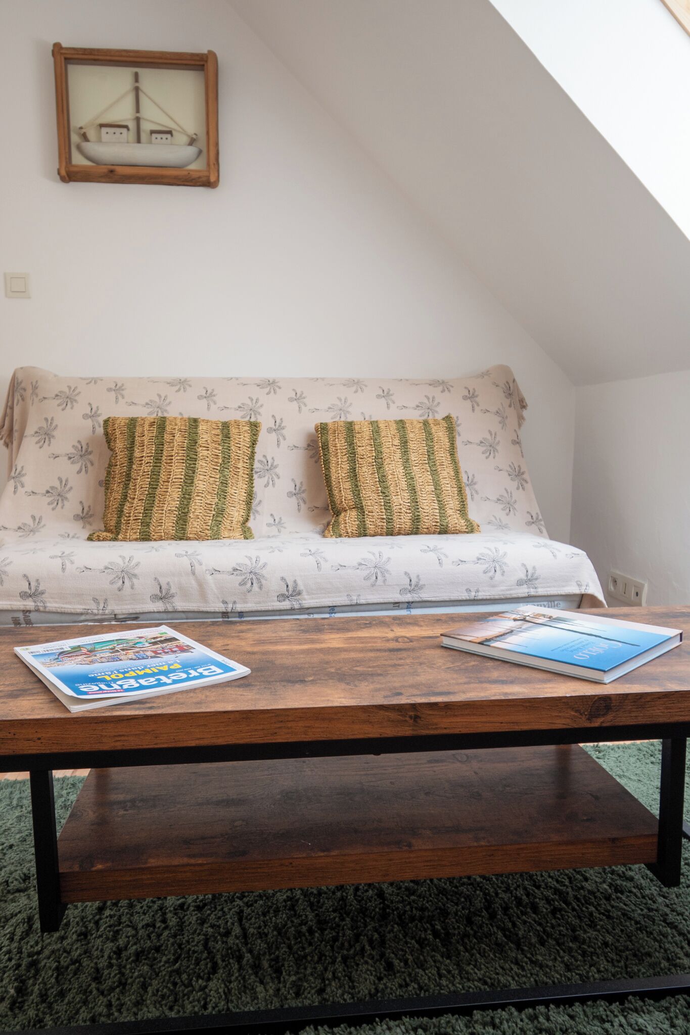 A cozy room with a sofa, two pillows, a wooden coffee table, and a framed picture on the wall.