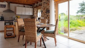Une cuisine rustique aux murs de pierre, aux poutres apparentes et dotée d’une grande porte-fenêtre coulissante donnant sur un jardin.
