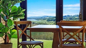 A wooden table and chairs with a view of a green landscape through large windows. - Goolara – luxurious two-storey escape with ensuite bedrooms, sauna and countryside views (Burrawang)
