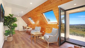 A cozy loft bedroom with wooden walls, a large skylight, a dining area, and a view of the countryside. - Goolara – luxurious two-storey escape with ensuite bedrooms, sauna and countryside views (Burrawang)