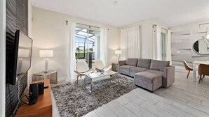 En moderne stue med en grå sofa, et glasbord og et fjernsyn på et træstel.