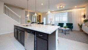 Une cuisine moderne dotée de plans de travail en granit, d’un lave-vaisselle encastré et de luminaires suspendus.