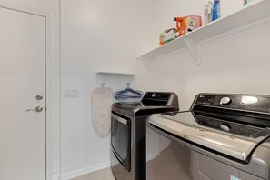 Un área de lavandería con lavadora y secadora, una puerta blanca y un estante con productos de limpieza.