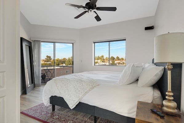 Un dormitorio moderno con una cama grande, un ventilador de techo y vistas a la ciudad a través de amplias ventanas.