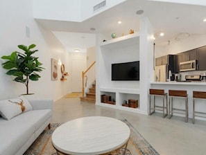 A modern living room with a sofa, a round coffee table, a TV, and a kitchen area with a microwave and bar stools. - Walk To All- Townhouse in Old Town Scottsdale Right Off Canal (Scottsdale)