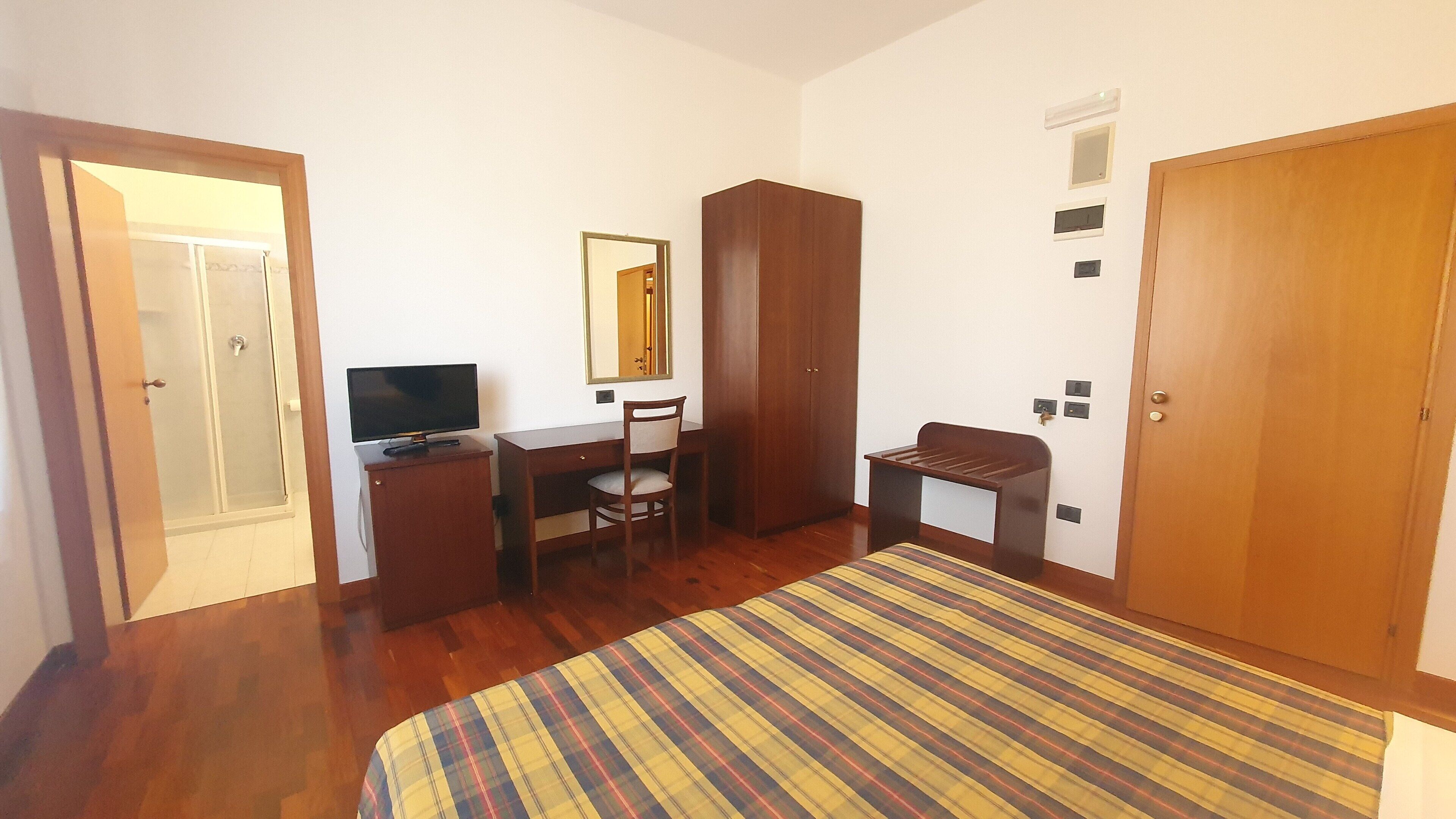 A bedroom with a bed, a desk, a chair, a wardrobe, and a television.