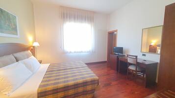 Habitación de hotel con una cama, un escritorio con computadora, una silla, una ventana con cortinas y un espejo en la pared.