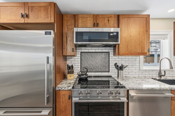 A kitchen with wooden cabinets, a stainless steel refrigerator, a microwave, a gas stove, and a dishwasher. - Kanons Kottage Downtown Retreat Near Rmnp (Loveland)