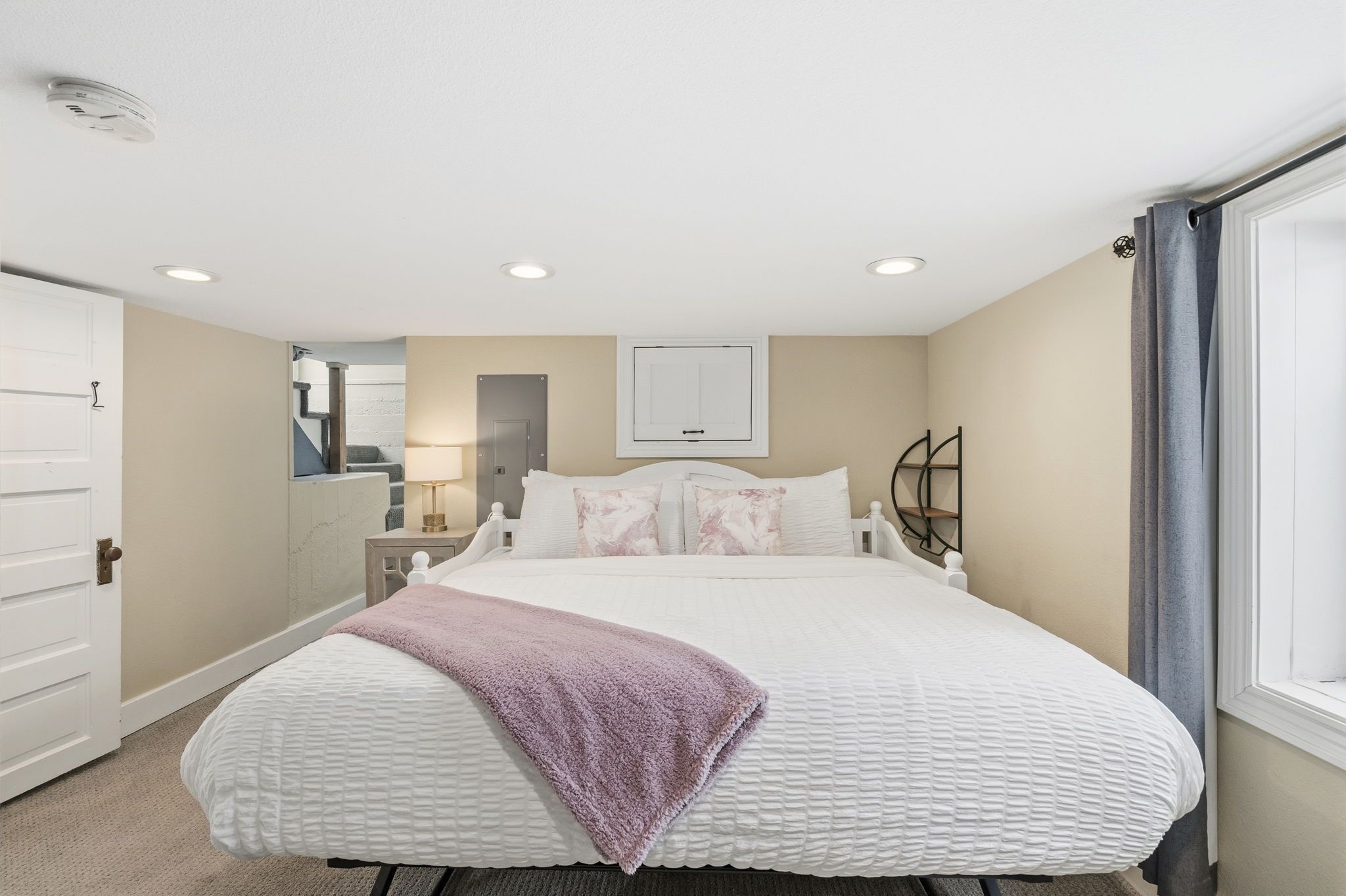 Une chambre à coucher avec un grand lit, une table de chevet, une commode, un miroir et une fenêtre avec des rideaux.