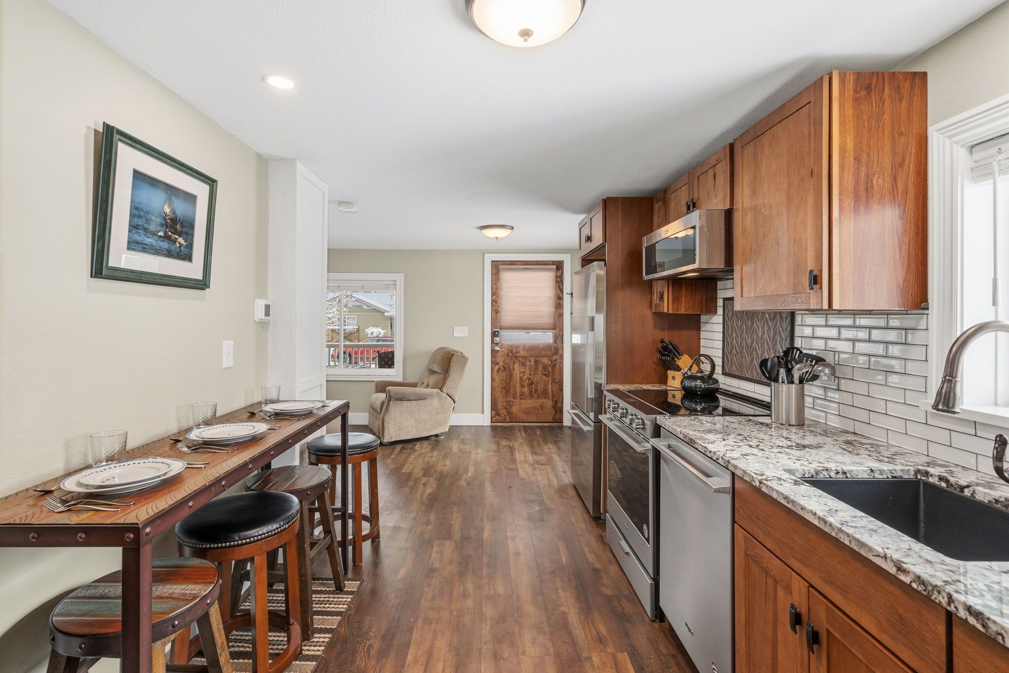 A kitchen with wooden cabinets, a granite countertop, and a dining area with a long table and bar stools.
