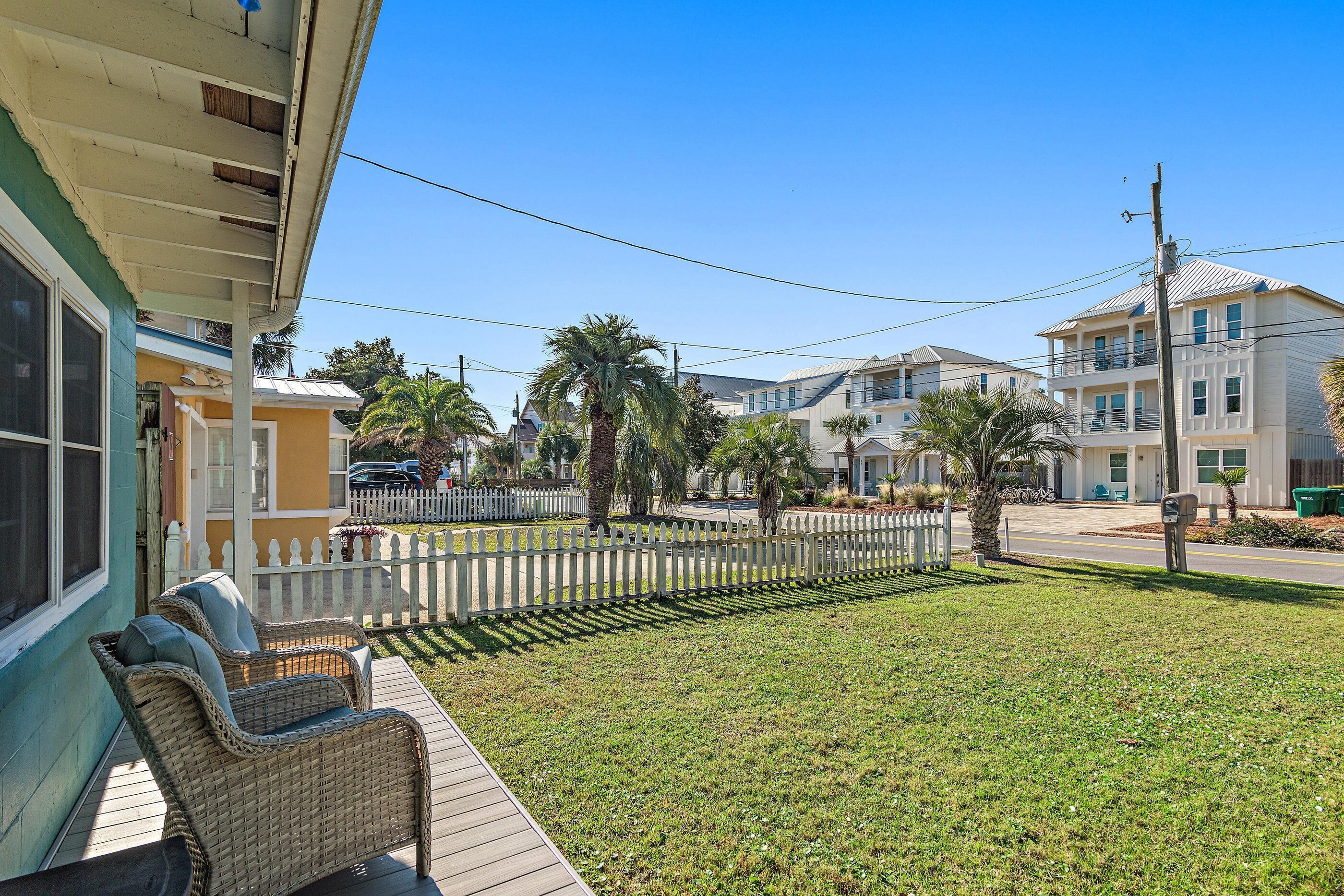 A residential area with a porch, wicker furniture, a white picket fence, and palm trees.