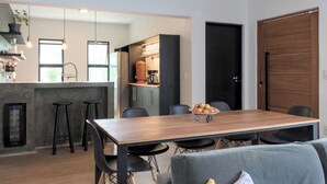 A modern kitchen with a wooden dining table, bar stools, and a grey sofa.