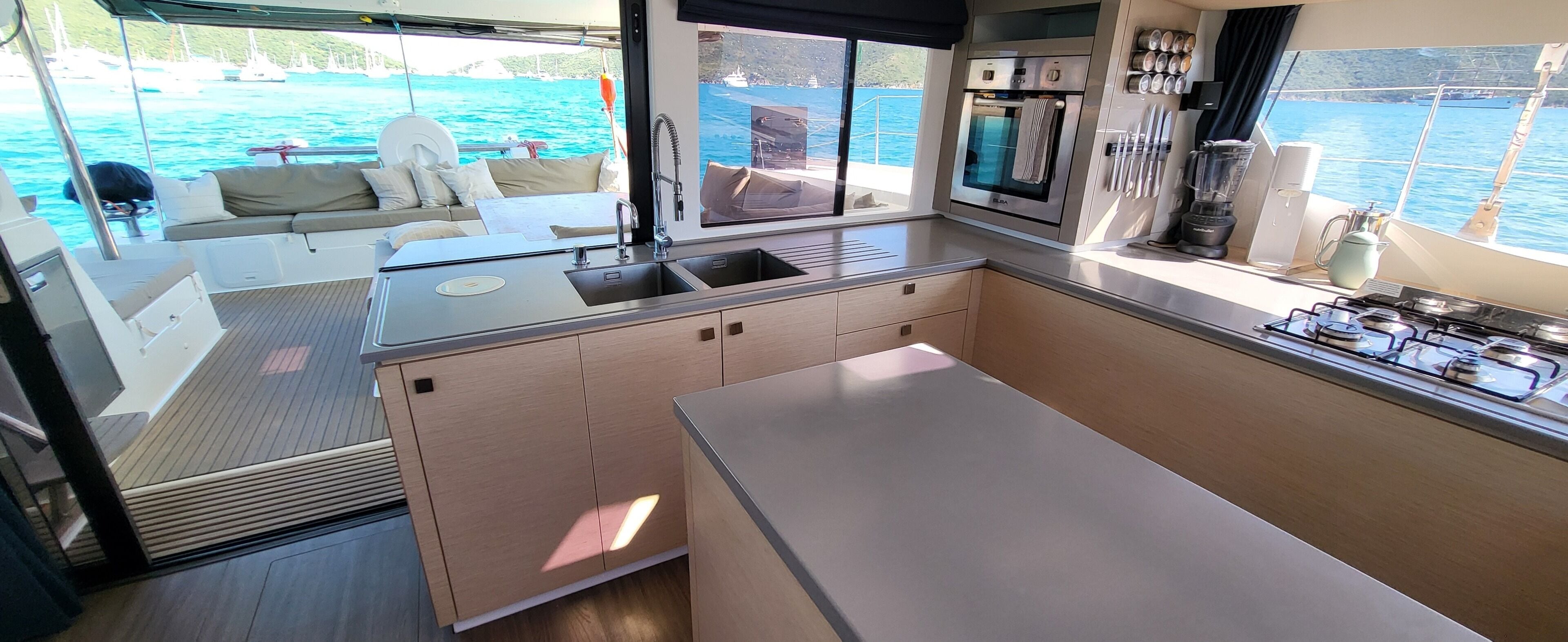 A compact galley kitchen with a sink, stove, and oven, overlooking a marina with boats.