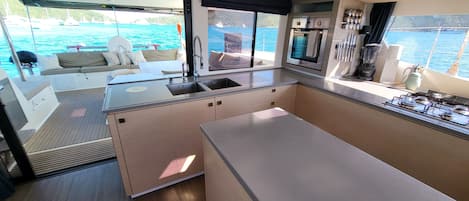 A compact galley kitchen with a sink, stove, and oven, overlooking a marina with boats.