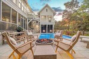 A poolside area with lounge chairs, a fire pit, and a view of a large house with a balcony. - Blue Water Haven|Private Heated Pool|Golf Cart|Newly Remodeled (Santa Rosa Beach)